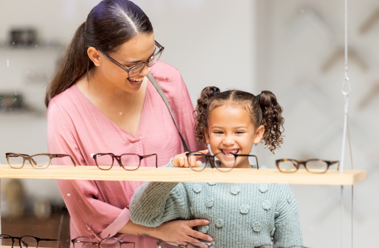 Child pointing at glasses on a store shelf next to their parent.