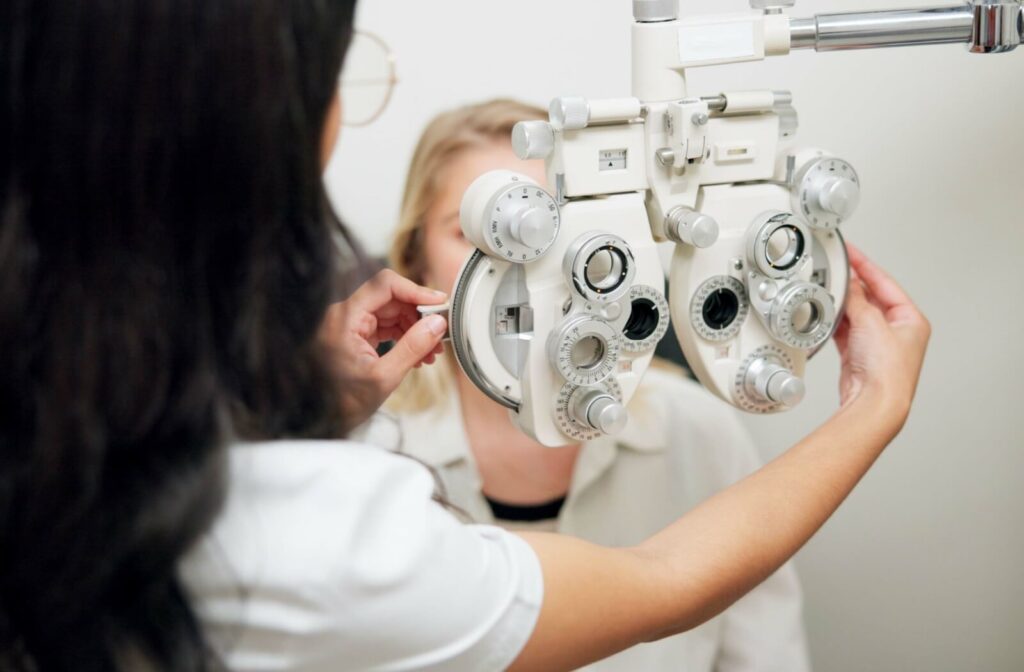 Optometrist adjusting a phoropter during an eye exam while a patient looks through the lenses in a bright clinic setting.