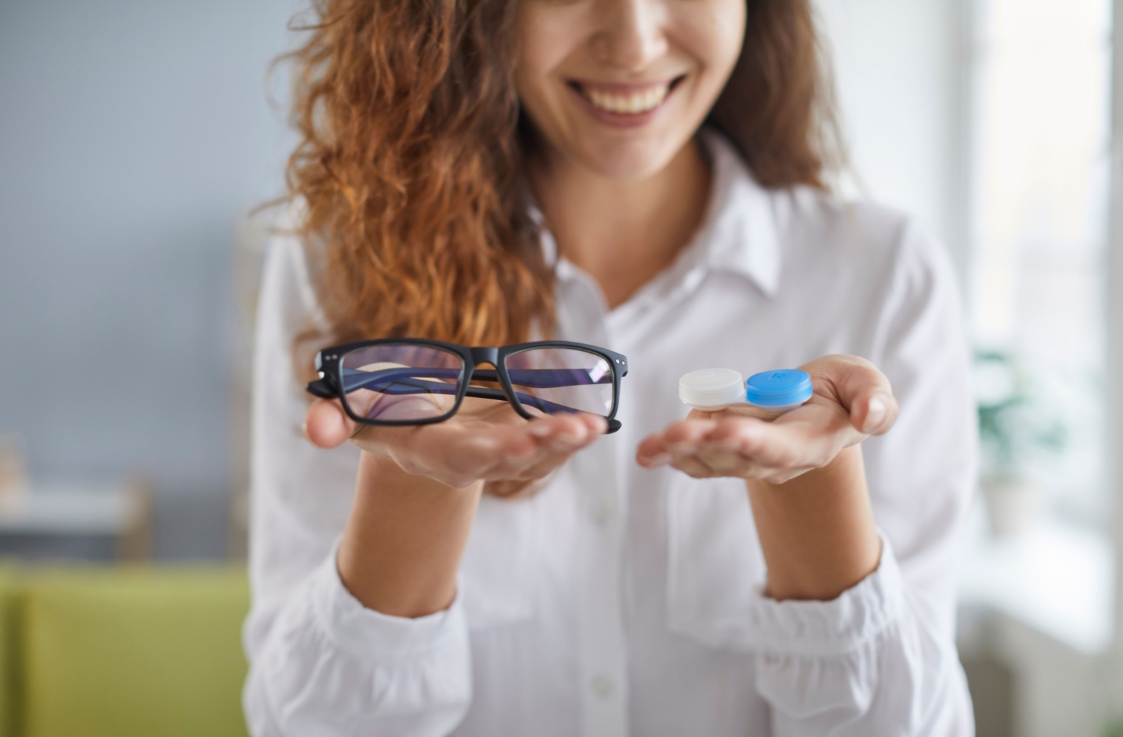 A person holding a pair of glasses in one hand and contact lenses in the other